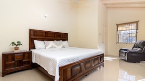 A bedroom with a wooden bed, a nightstand with drawers, a potted plant, and a window with bars. - Lot 40 Draxhall  (St. Ann's Bay)