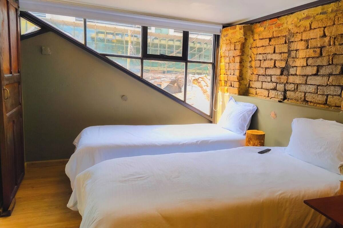 A room with two beds, a brick wall, and a window overlooking construction.