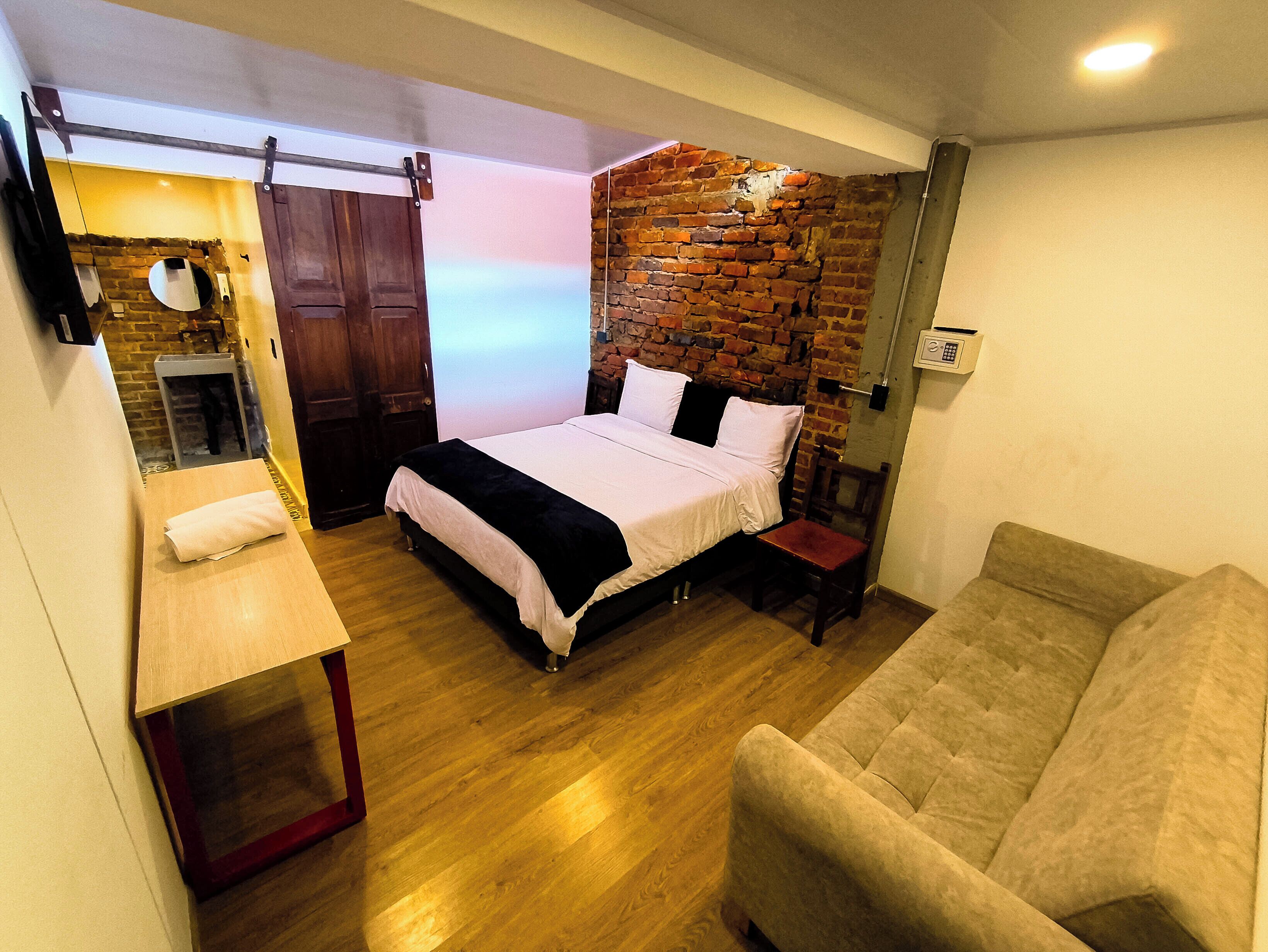 A bedroom with a bed, a wooden bench, a brick wall, and a couch.