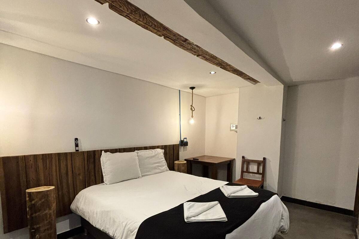 A modern bedroom with a large bed, wooden headboard, bedside tables, and a small wooden stool.