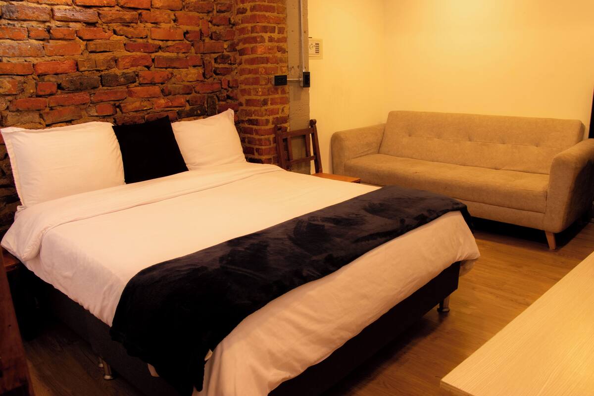 A room with a bed, a sofa, and a brick wall.
