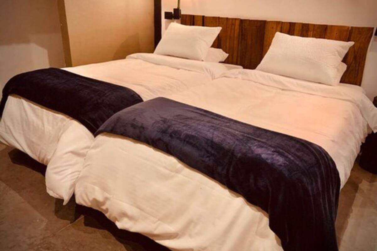 A double bed with a wooden headboard, white bedding, and two dark blue throw pillows.
