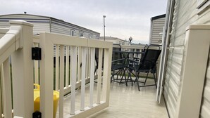 A deck area with a white railing, a yellow chair, and a black chair.