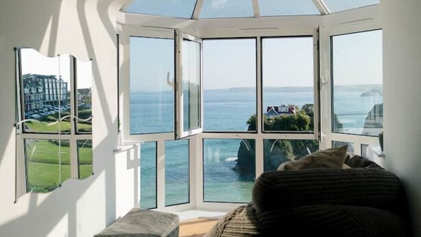 A room with a bay window overlooking the sea, a bed, and a view of a coastal landscape. - Spectacular Sea View Penthouse Apartment + Parking (Newquay)