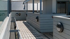 A covered outdoor area with a wooden deck, metal railings, and a small enclosed seating area with a window. - Spectacular Sea View Penthouse Apartment + Parking (Newquay)