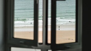 Uitzicht door een raam op een strand, met de oceaan en een zandstrand.