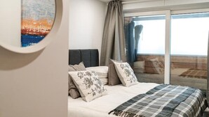Een slaapkamer met een bed, een nachtkastje, een groot raam met gordijnen en een schilderij aan de muur.