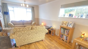 A living room with a patterned sofa, a wooden coffee table, a bookshelf, and a chandelier. - 3 Bedroom House, Hot Tub,torbay, Sleeps 6, Parking (Newton Abbot)