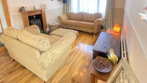 A living room with a sofa, a chair, a fireplace, and a table with decorative items. - 3 Bedroom House, Hot Tub,torbay, Sleeps 6, Parking (Newton Abbot)