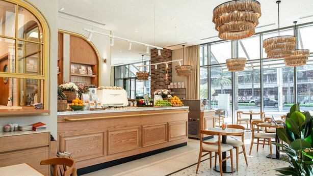 A modern cafe with a wooden counter, seating area, and large windows offering a view of the street.