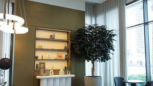 A modern lobby with a large potted tree, a reception desk, and a seating area.
