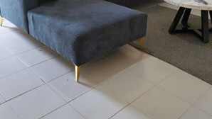 Un salon moderne avec un canapé d’angle gris, deux coussins rouges et une table basse ronde sur laquelle se trouve une télécommande.