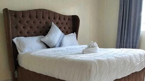 Un lit bien fait, avec une tête de lit marron, du linge de lit blanc et une serviette pliée posée sur le côté.