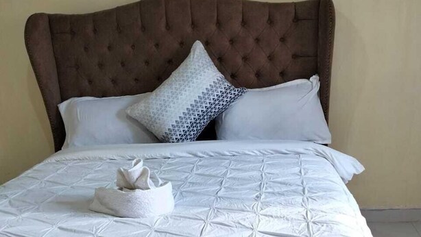 Un lit bien fait, avec une tête de lit capitonnée, du linge de lit blanc et une serviette pliée posée sur le lit.