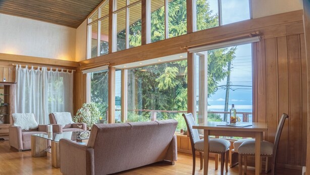 A spacious living room with a large window, a sofa, chairs, and a table. - Amadeus Hotel (Frutillar)