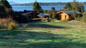 A residential area with two houses, a grassy field, and a lake with mountains in the background. - Amadeus Hotel (Frutillar)