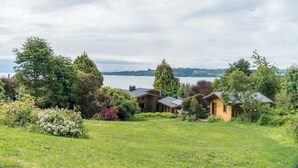 A lakeside property with a main house and a smaller cabin, surrounded by lush greenery and trees. - Amadeus Hotel (Frutillar)