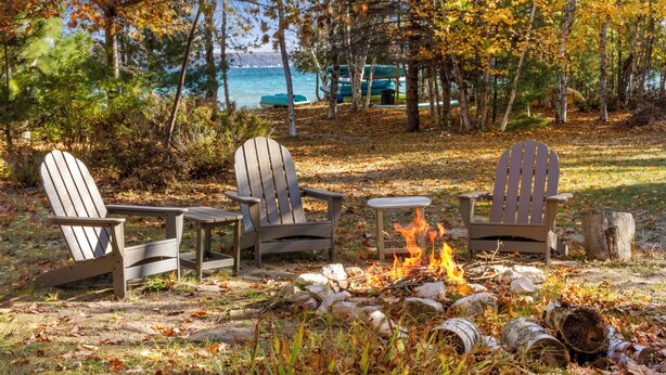 A campfire with Adirondack chairs around it, a log fire pit, and a view of a lake with boats in the background. - Lower Terrace in Three Pines Resort (Frankfort)