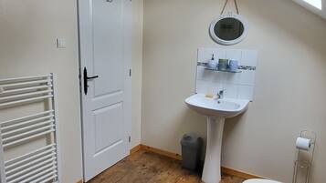 A small, compact bathroom with a white door, a white pedestal sink, a toilet, a wooden floor, and a skylight.