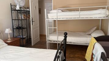 A room with bunk beds, a bedside table with a lamp, a fan, and a door leading to another room.