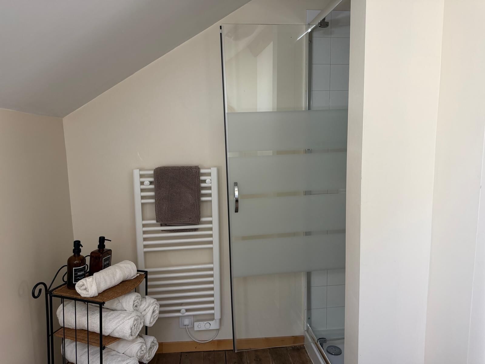 A bathroom with a glass shower enclosure, a towel rack with folded towels, and a shelf with toiletries.