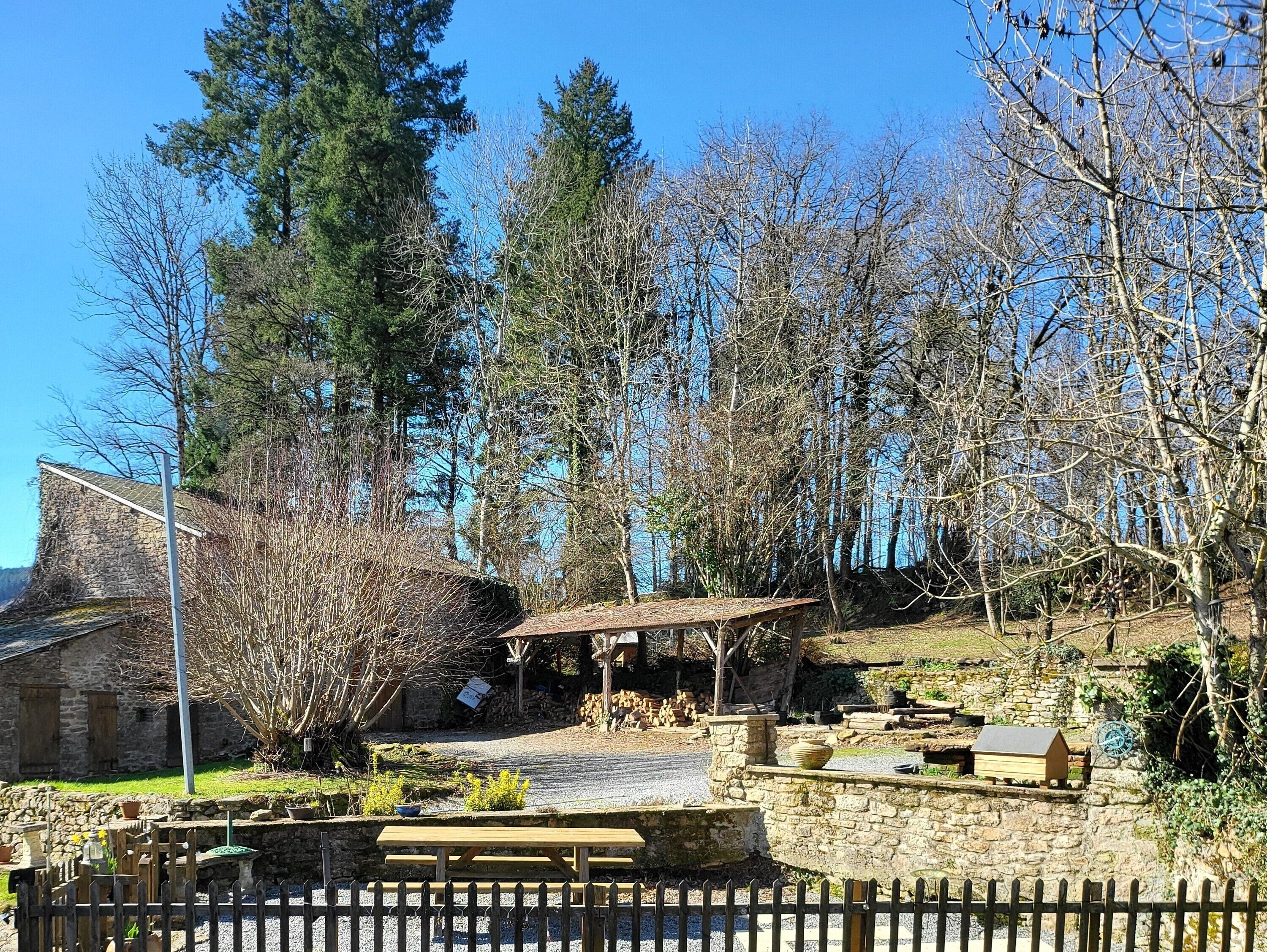 A rustic outdoor area with a stone wall, wooden benches, and a picnic table.