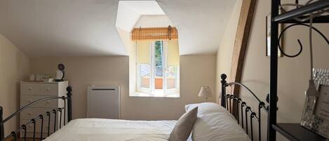 A bedroom with a bed, a window with a view, a desk, and a radiator.