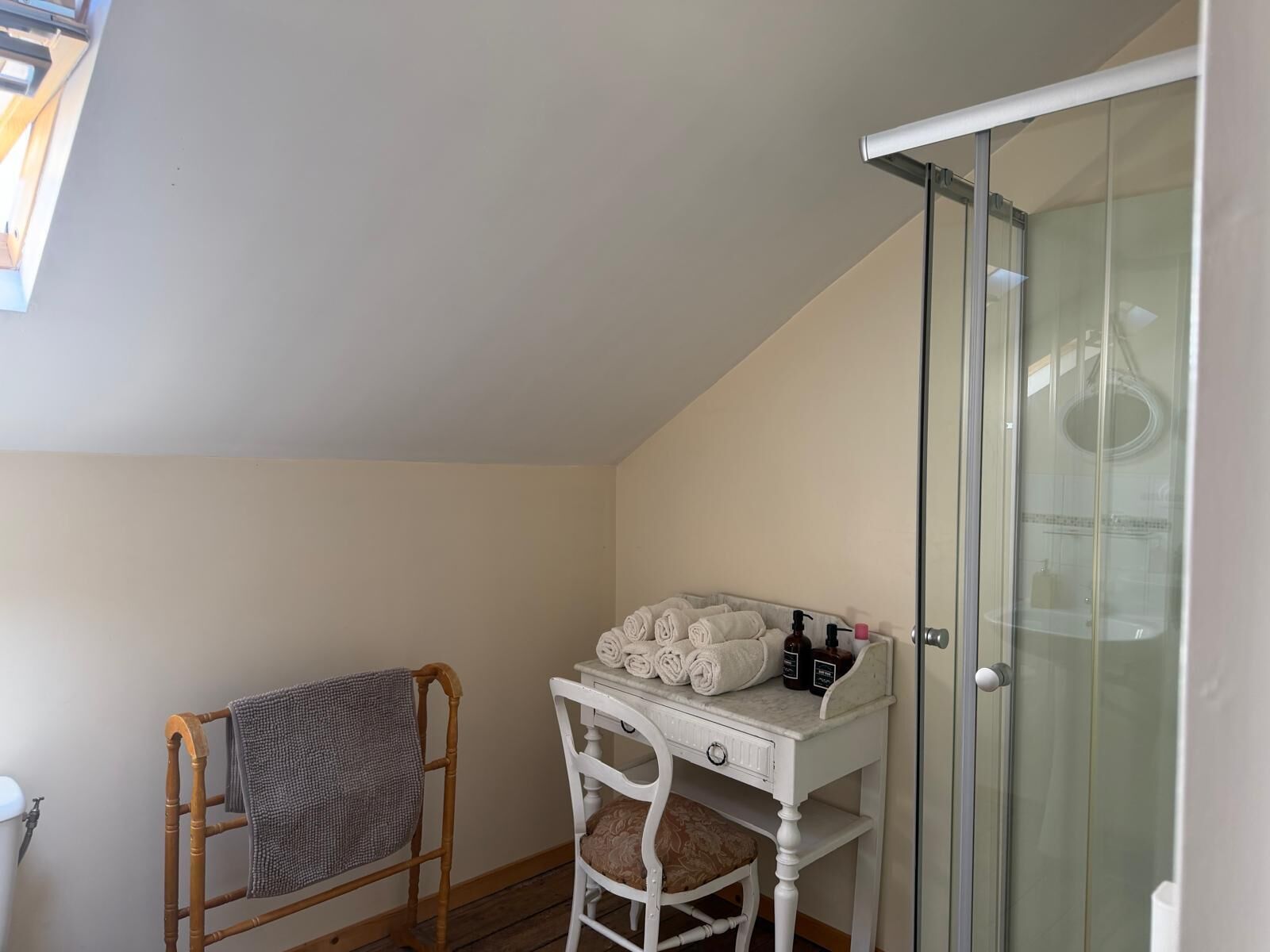 Une salle de bain équipée d’une douche, d’un porte-serviettes, d’un meuble-lavabo avec des articles de toilette et d’une chaise.