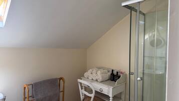 Une salle de bain équipée d’une douche, d’un porte-serviettes, d’un meuble-lavabo avec des articles de toilette et d’une chaise.