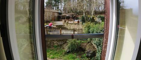 A view through a window of a garden area with a wooden fence, a stone wall, and a small pond.