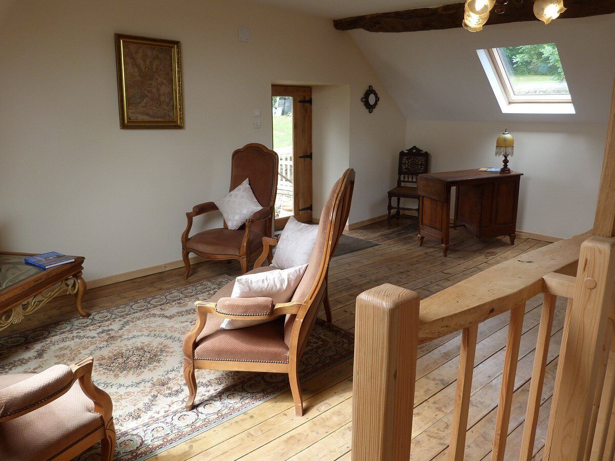 A cozy room with a wooden floor, a large window with a view, a wooden chair, a small table, and a bookshelf.