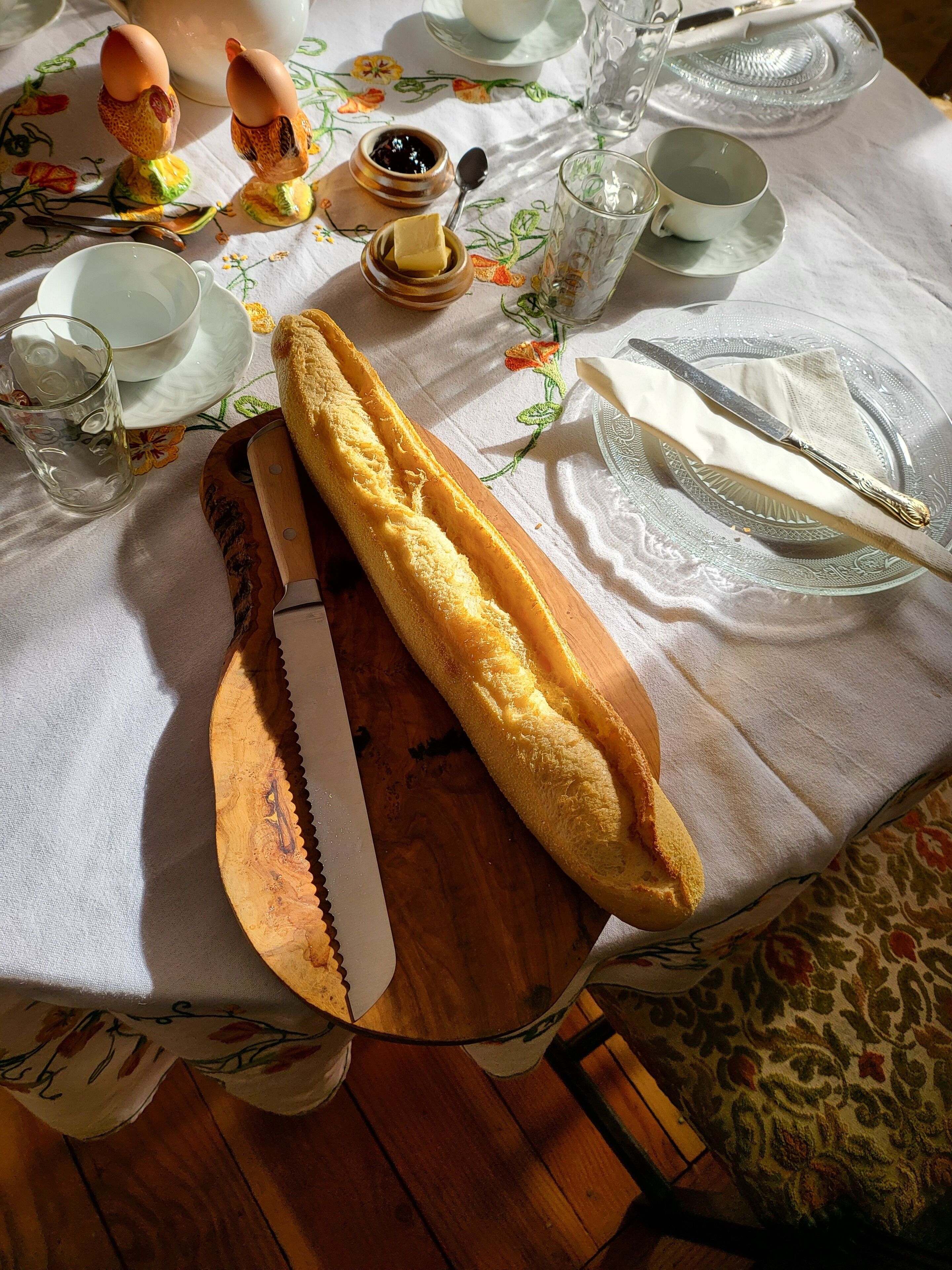 Ein Tisch gedeckt mit einem Baguette, einem Messer, einem Glas und einer Tasse.