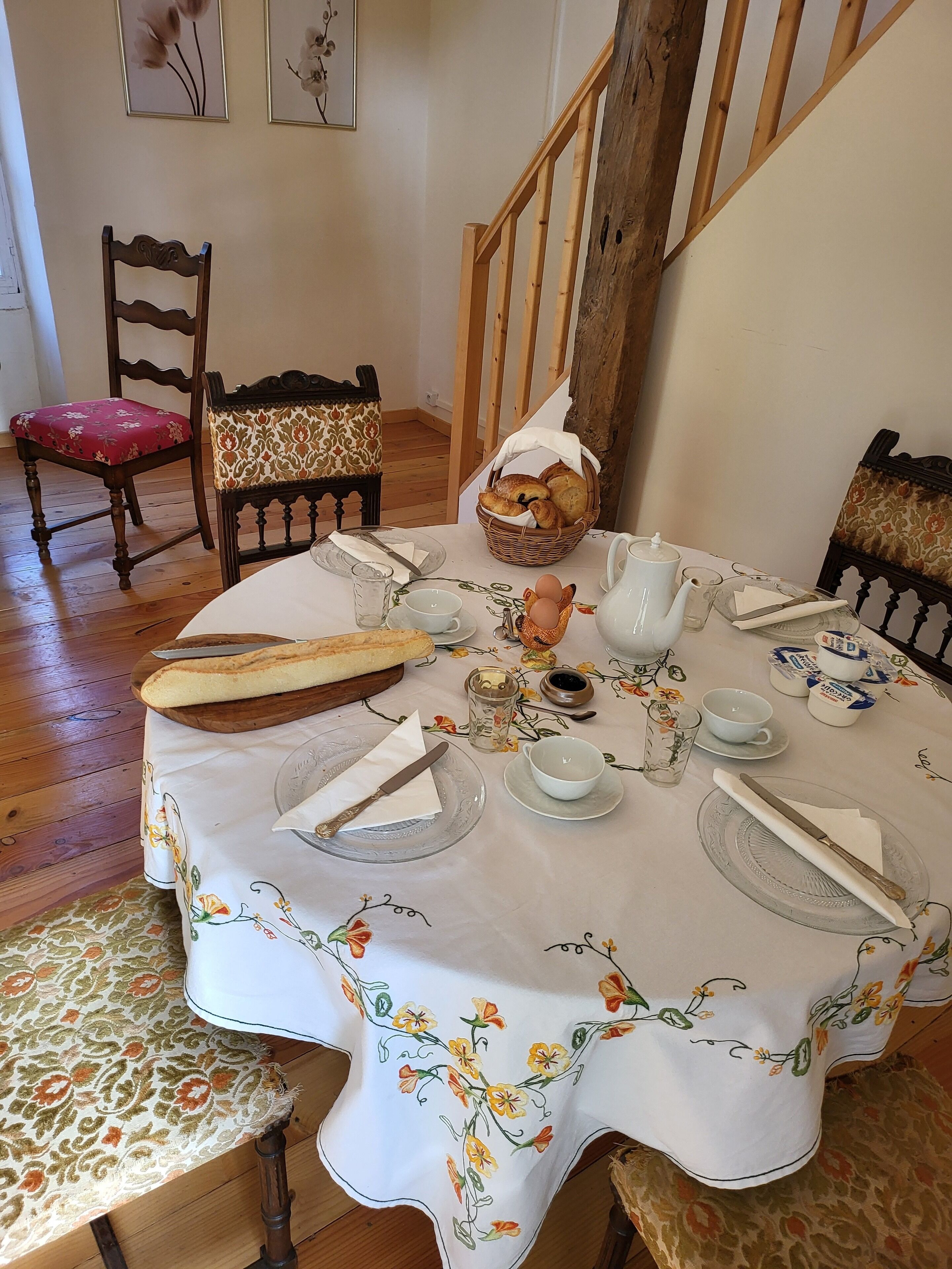 Une table à manger dressée avec des assiettes, des couverts, un panier de pain et une carafe.