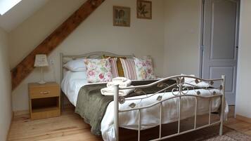 A bedroom with a sloped ceiling, a bed with floral bedding, a bedside table, and a door.