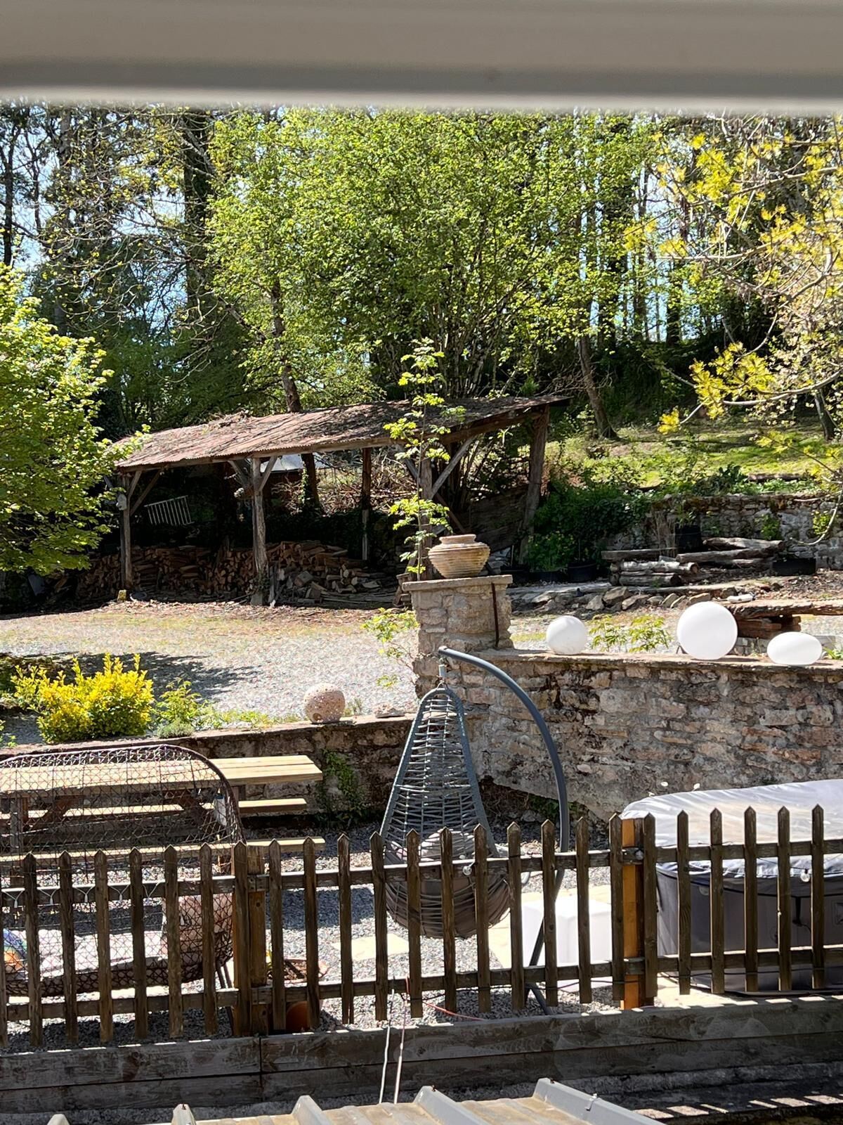 A rustic outdoor area with a wooden pergola, stone walls, and a metal spiral structure.
