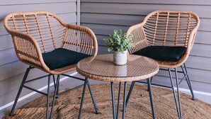 Two wicker chairs with black cushions and a small table with a potted plant between them.