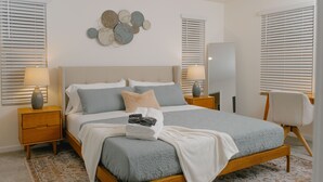 A neatly made bed with a grey and white duvet, a bedside table with a lamp, and a decorative wall piece.