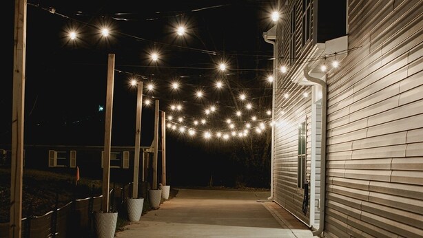 A pathway leading to a building with string lights overhead.