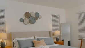 A neatly arranged bedroom with a bed, bedside tables, a mirror, and a decorative wall piece.