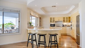 A modern kitchen with a central island, bar stools, and a view of the outdoors. - Anchors at Mollymook Beach (Mollymook)