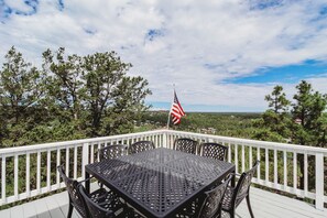 A deck with a table and chairs, an American flag, and a view of trees and a distant landscape.
