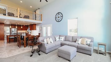 A spacious living room with a grey sectional sofa, a dining area with wooden furniture, and a balcony with a railing.
