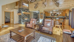 A spacious living room with leather chairs, a fireplace, and a stone wall.