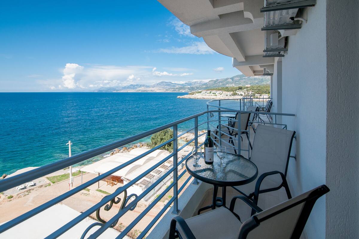 A balcony with a table and chairs overlooking a coastal view.