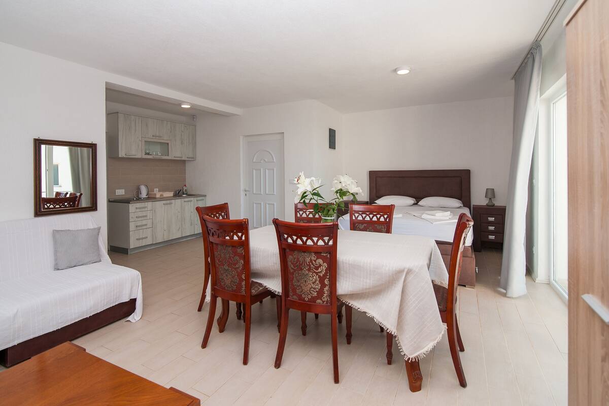 A hotel room with a dining area, a bed, a kitchen, and a bathroom.