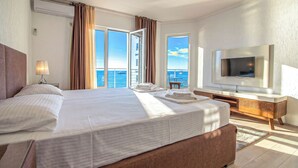 Une chambre d’hôtel avec un grand lit, une télévision, un balcon avec des rideaux et une vue sur la mer.