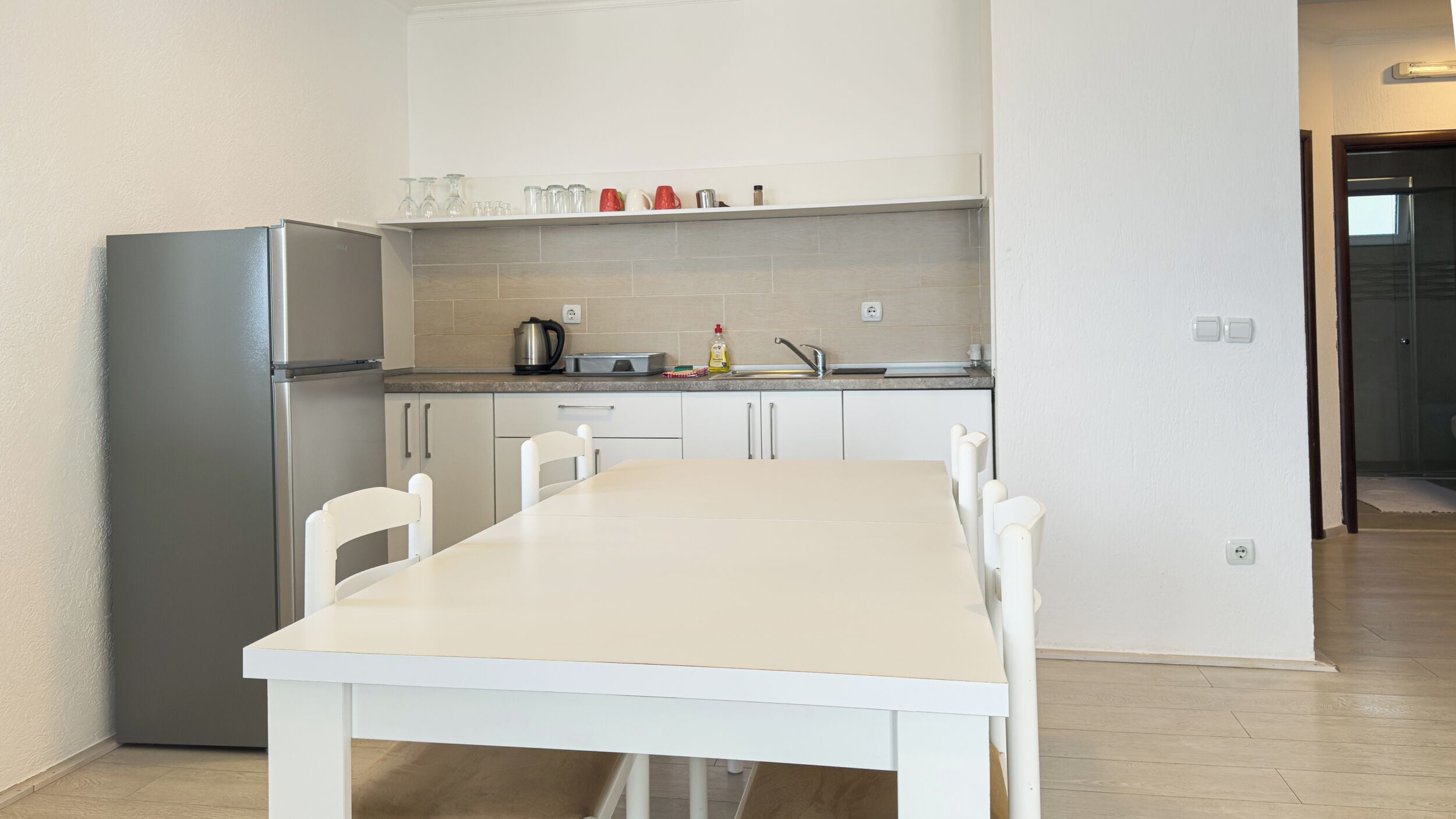 A modern kitchen with a white table and chairs, a refrigerator, and a countertop with various kitchen items.