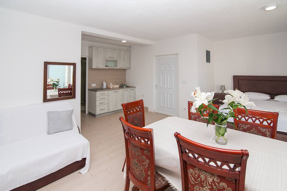 A hotel room with a bed, a dining table with chairs, a kitchen area, and a bathroom visible through an open door.