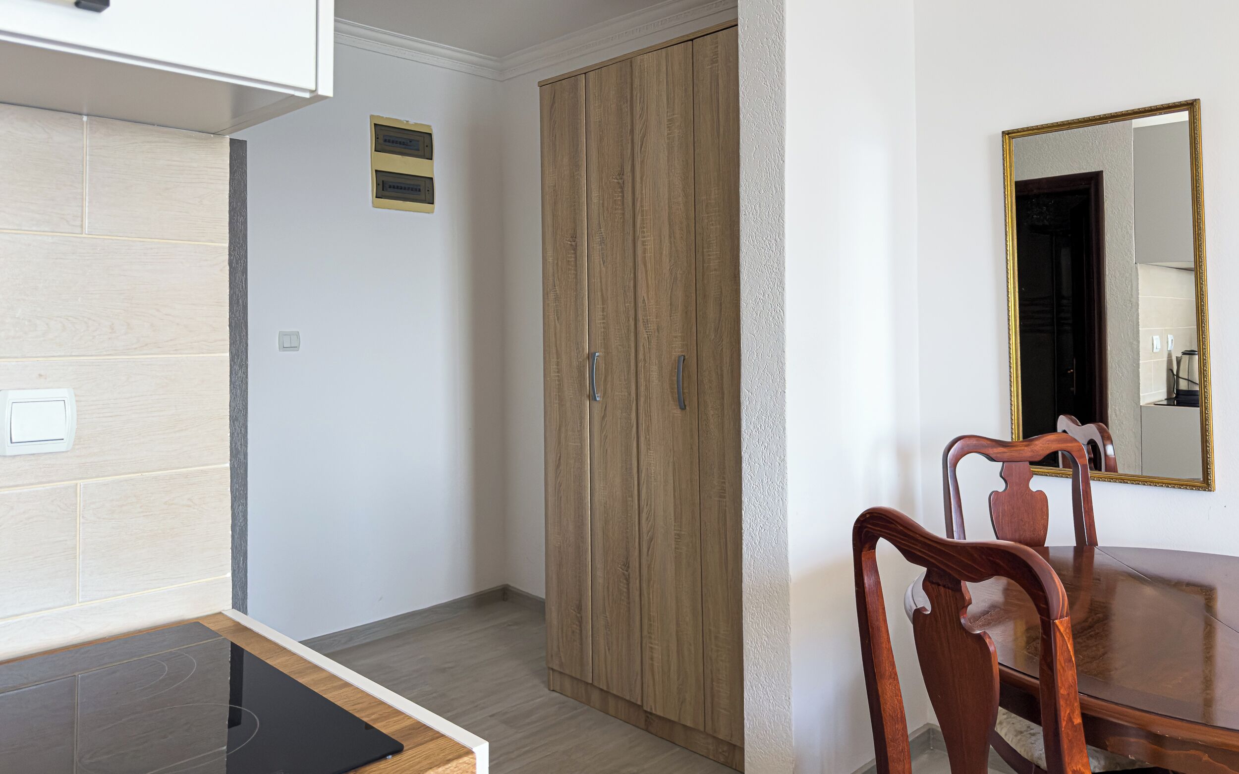 A room with a wooden wardrobe, a dining table with chairs, and a mirror on the wall.