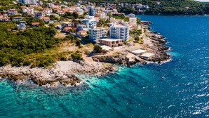 Vue aérienne d’une ville côtière, avec des bâtiments le long du littoral, une eau d’un bleu limpide et un paysage rocheux.